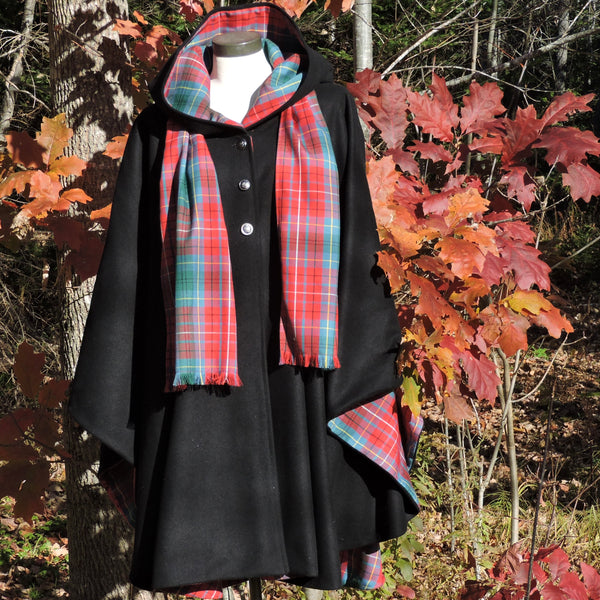 A black hooded cape with a BC tartan and matching lining, displayed on a mannequin outdoors in front of autumn trees.