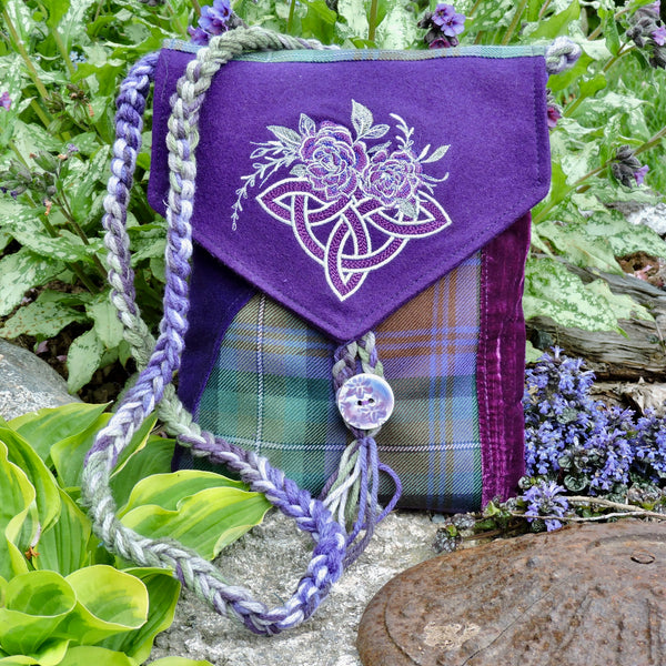 Purple bag with floral design and tartan pattern, surrounded by greenery and flowers.